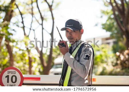 Middle year of Asian Male Security Guard Talking a portable wireless transceiver in village  entrance . Security guard opening The entrance to the village door. Speed 10 limit in area, copy space. 