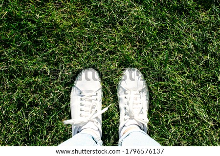 Legs in white sneakers and blue jeans are on the grass.