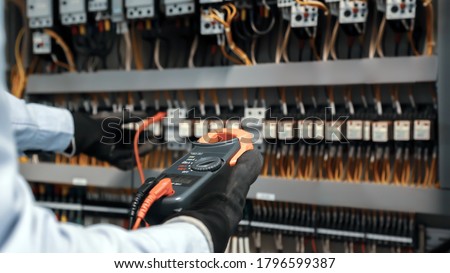 Electrical engineer using digital multi-meter measuring equipment to checking electric current voltage at circuit breaker and cable wiring system in main power distribution board. Royalty-Free Stock Photo #1796599387