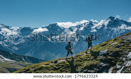 Two young hikers (a couple) walking up a mountain in Austria in summer, with scenic snow covered mountains on the background Royalty-Free Stock Photo #1796623324