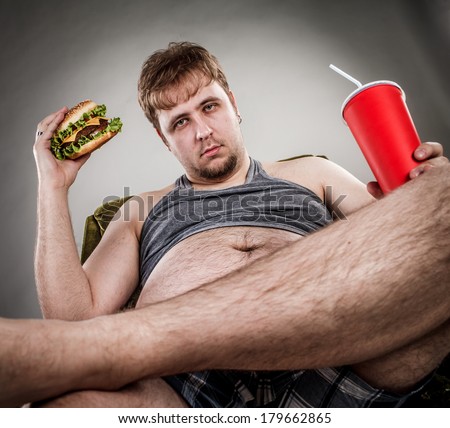 Fat man eating hamburger seated on armchair. Style fast food.