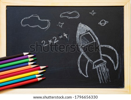 Back to school concept with hand drawn rocket on blackboard and school supplies. Flat lay.
