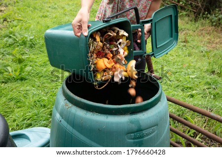 A woman emptying a home composting bin into an outdoor compost bin to reduce waste Royalty-Free Stock Photo #1796660428