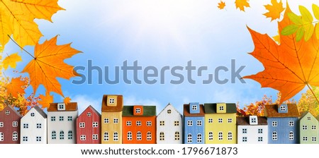 Colorful miniature house in a row on blue sky and autumn leaves background. Fall City skyline background web banner.