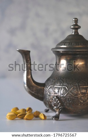 Vintage metal teapot on a white table and a handful of yellow pistachios