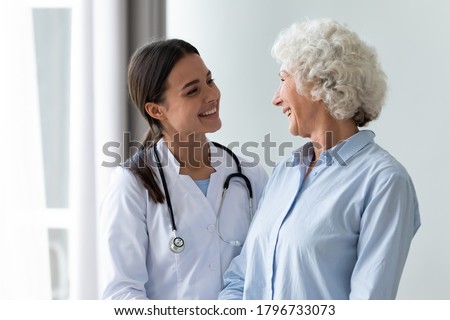 Smiling young female general practitioner enjoying sincere talk, sharing good health news with hoary older senior woman indoors. Caring millennial nurse helping middle aged patient at meeting. Royalty-Free Stock Photo #1796733073