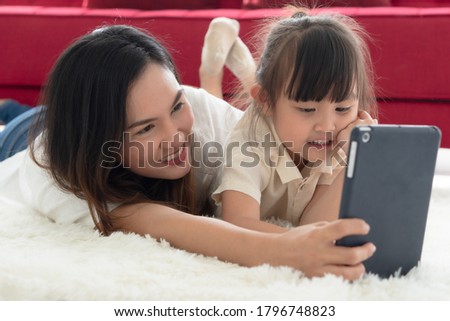 asian beautiful mother lying on the carpet and watching cartoon in tablet with her young daughter. family together and relationship