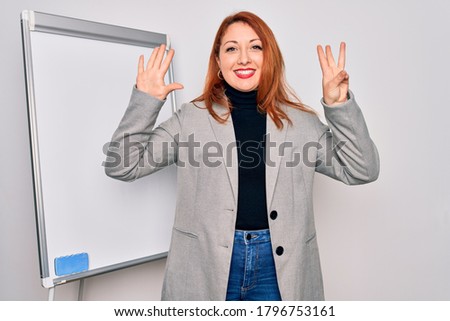 Young beautiful redhead businesswoman doing business presentation using magnetic board showing and pointing up with fingers number eight while smiling confident and happy.