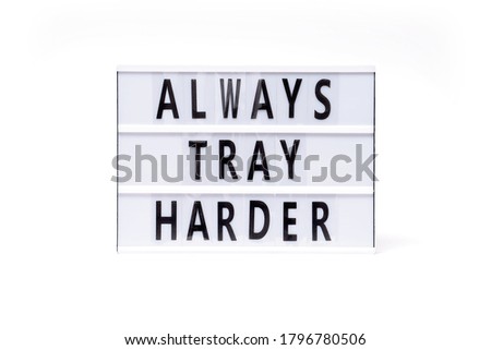Always tray harder. Text on a vintage lightbox display placed on a white table on a light background.                       