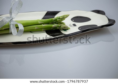 A bunch of fresh asparagus lies on a plate with a picture of a panda bear on a white background.