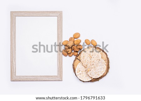 Still life of organic products. Empty wooden picture frame. Walnuts, organic rice bread stacked on a round piece of wood. Everything is placed on a bright table. Flat, top view, no people