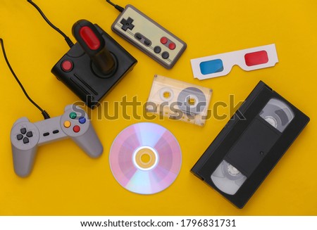 Flat lay 80s attribute composition. Gamepads, audio and video tapes, CD, 3D glasses. Retro Electronics, gadgets and devices. Entertainment and gaming. Yellow background. Top view