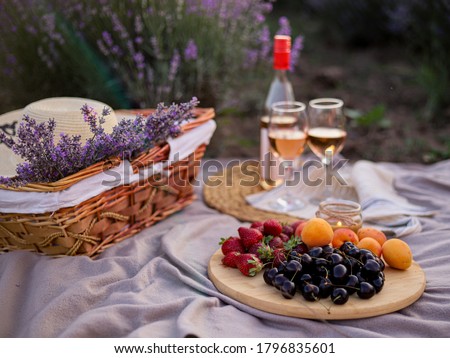 Romantic picnic in nature with fruits, berries and white wine. A bouquet of Lavanda, a straw hat and a candle decorate the picnic. Front view.