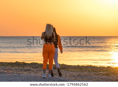 Two young women on the beach at sunrise. One girl is blonde and the other is brunette. Vacation
