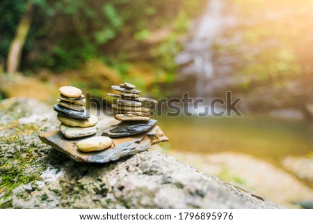 Rock stones stacking resting on top of each other representing balance support and structure foundation meditation peaceful, waterfall in background in rainforest jungle nature exploration adventure 