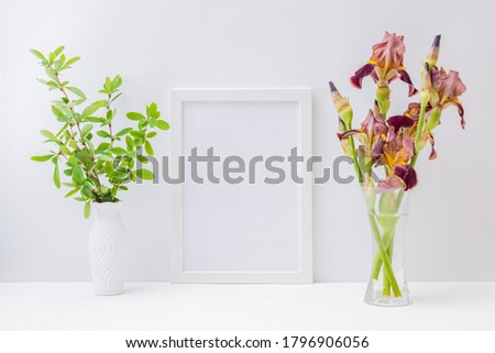 Home interior with decor elements. Mockup with a white frame and bouquet of irises flowers in a glass vase on a light background