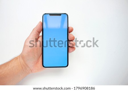 A person holding an Smart Phone with a blue sky screen on a white background.