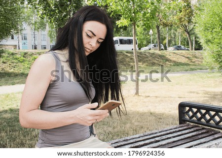 photo of a woman of European appearance sitting on a bench and holding a phone in one hand
