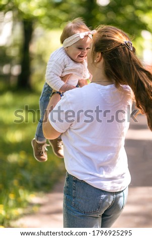 A young mother walks with a one-year-old baby, holds him in her arms, hugs. Communication with the child for his harmonious development