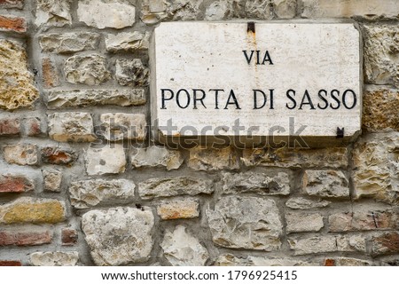 Close up of an old stone wall with a street sign that says: "Stone Gate Street" (from Italian: "Via Porta di Sasso"), Castell'Arquato, Italy