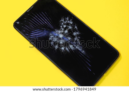 A cell phone with a broken heart-shaped screen on a yellow background.