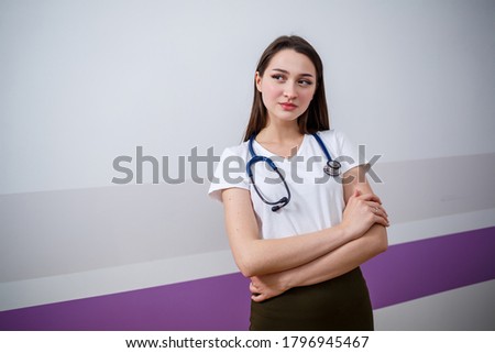 A girl of European appearance with a phonendoscope on her neck. Attractive young brunette woman smiles. She is a young doctor, intern student