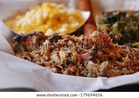 A serving of pulled pork with side dishes of Macaroni and cheese,  collard greens, and fried hush puppies. Royalty-Free Stock Photo #179694656