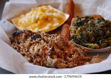 A serving of pulled pork with side dishes of Macaroni and cheese,  collard greens, and fried hush puppies. Royalty-Free Stock Photo #179694659