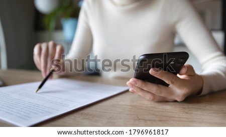 Close up focused financier reading paper contract agreement, checking latest investment news in smartphone application indoors, concentrated female editor reading document or report at workplace. Royalty-Free Stock Photo #1796961817