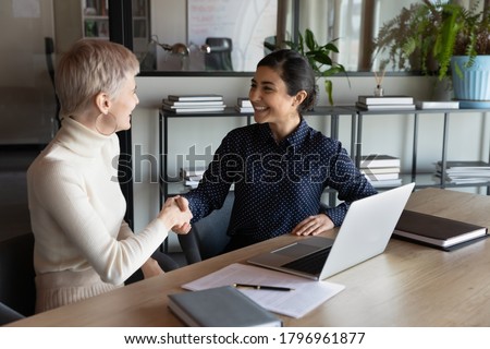 Happy two young mixed race business women shaking hands, making agreement deal in office. Smiling indian manager celebrating cooperation establishment with 30s blonde female partner at meeting. Royalty-Free Stock Photo #1796961877