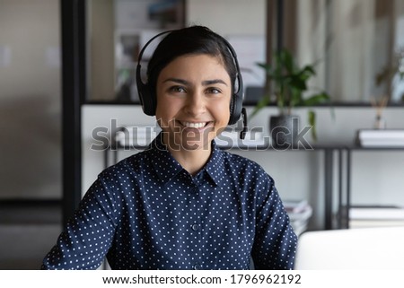Head shot portrait of pleasant smiling young indian ethnicity attractive female employee wearing wireless headset with mic, professional consultant advisor hotline specialist looking at camera. Royalty-Free Stock Photo #1796962192