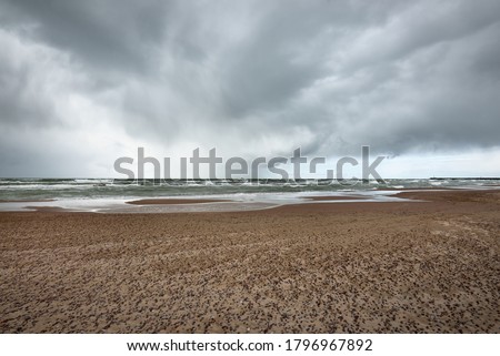 Sandy shore of the Baltic sea under the dramatic clouds after thunderstorm. Ventspils, Latvia. Epic seascape. Cyclone, gale, storm, rough weather, meteorology, climate change, natural phenomenon Royalty-Free Stock Photo #1796967892