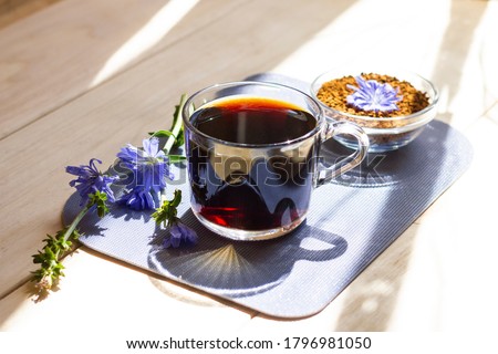 Hot natural chicory caffeine free drink in a transparent cup on a wooden table outdoors. Healthy alternative replacement for coffee, caffeine. Blue chicory flower. Beautiful summer morning at nature Royalty-Free Stock Photo #1796981050