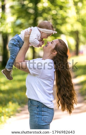 A young mother fools around and laughs with her one-year-old baby on a walk. Close communication with the child and trust