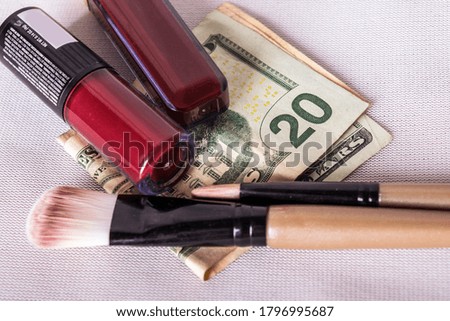Dollar bills on a flat surface with make up brushes and lipsticks on them.