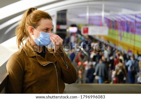 A young woman puts on a medical mask in the subway. Crowds of people going to the station Royalty-Free Stock Photo #1796996083