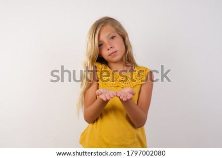 Little girl with beautiful blonde hair over white background holding something with open palms, offering to the camera.