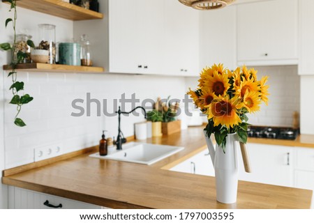 View on clean white simple modern kitchen in scandinavian style, kitchen details, wooden table, sunflowers bouquet in vase on the table