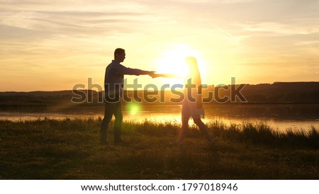 Young free couple dancing at sunset on beach. Happy guy and girl waltz in evening in a summer park. Enamored man and woman dance in the bright rays of the sun on background of the lake.