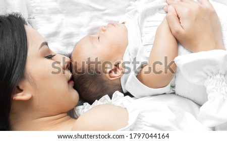 Portrait of enjoy happy love family asian mother playing with adorable little asian baby.Mom kiss with cute son moments good time in a white bedroom.Love of family concept