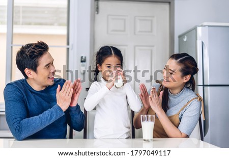 Portrait of enjoy happy love asian family father and mother  with little asian girl smiling and having breakfast drinking and hold glasses of milk at table in kitchen Royalty-Free Stock Photo #1797049117
