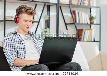 Teenage boy listening to music in headphones when working or playing game on laptop Royalty-Free Stock Photo #1797110341
