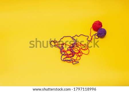a tangles of red and blue woolen threads lies unraveled on a yellow background. the view from the top