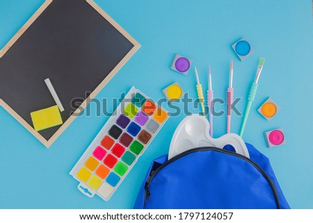 School, stationery poured from a blue backpack or knapsack on a light background, next to a school graphite board. Learning after vacation and quarantine. Place for text