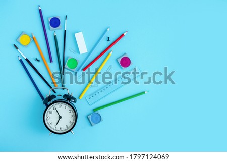 Stationery, crayons, brushes and paints around a black alarm clock. Back to school, start of the school year. Copy space