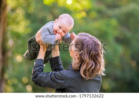 Portrait of a happy young mother with a half-year-old baby in her arms in the summer outdoors in the park. Mom and baby are smiling.