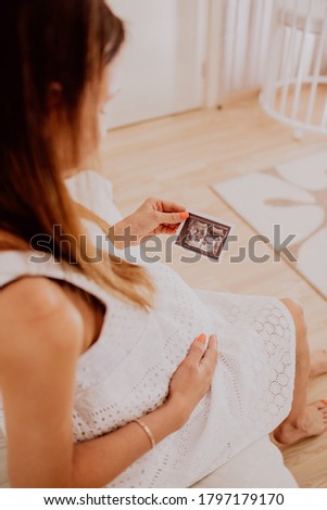 Pregnant woman looking at her baby twins sonography. Happy expectant mother enjoying first photo of her kids, face is unrecognizable