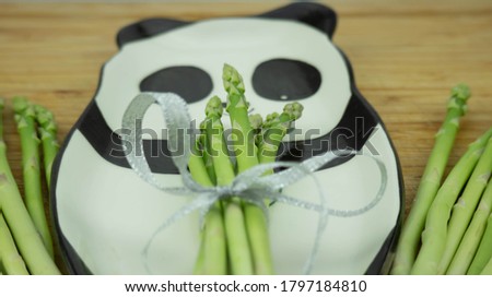 A bunch of fresh asparagus lies on a plate with a picture of a panda bear. On a wooden cutting board.