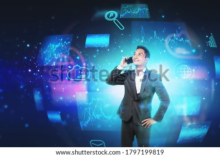 Cheerful young Asian businessman talking on smartphone with double exposure of blurry immersive cloud computing interface. Toned image