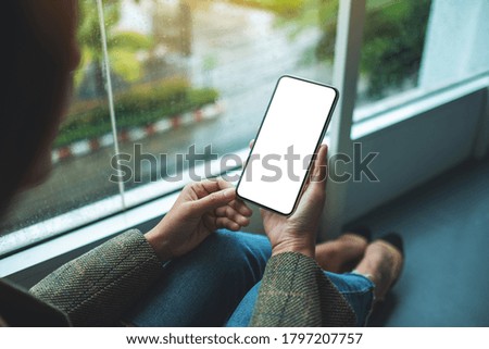 Mockup image of a woman holding  mobile phone with blank white desktop screen while sitting on the floor